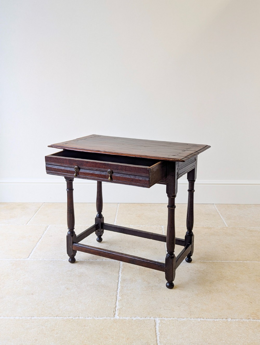 A late 17th-century dark oak side table with turned legs, lower stretchers, and a single drawer featuring brass drop handles. View IV