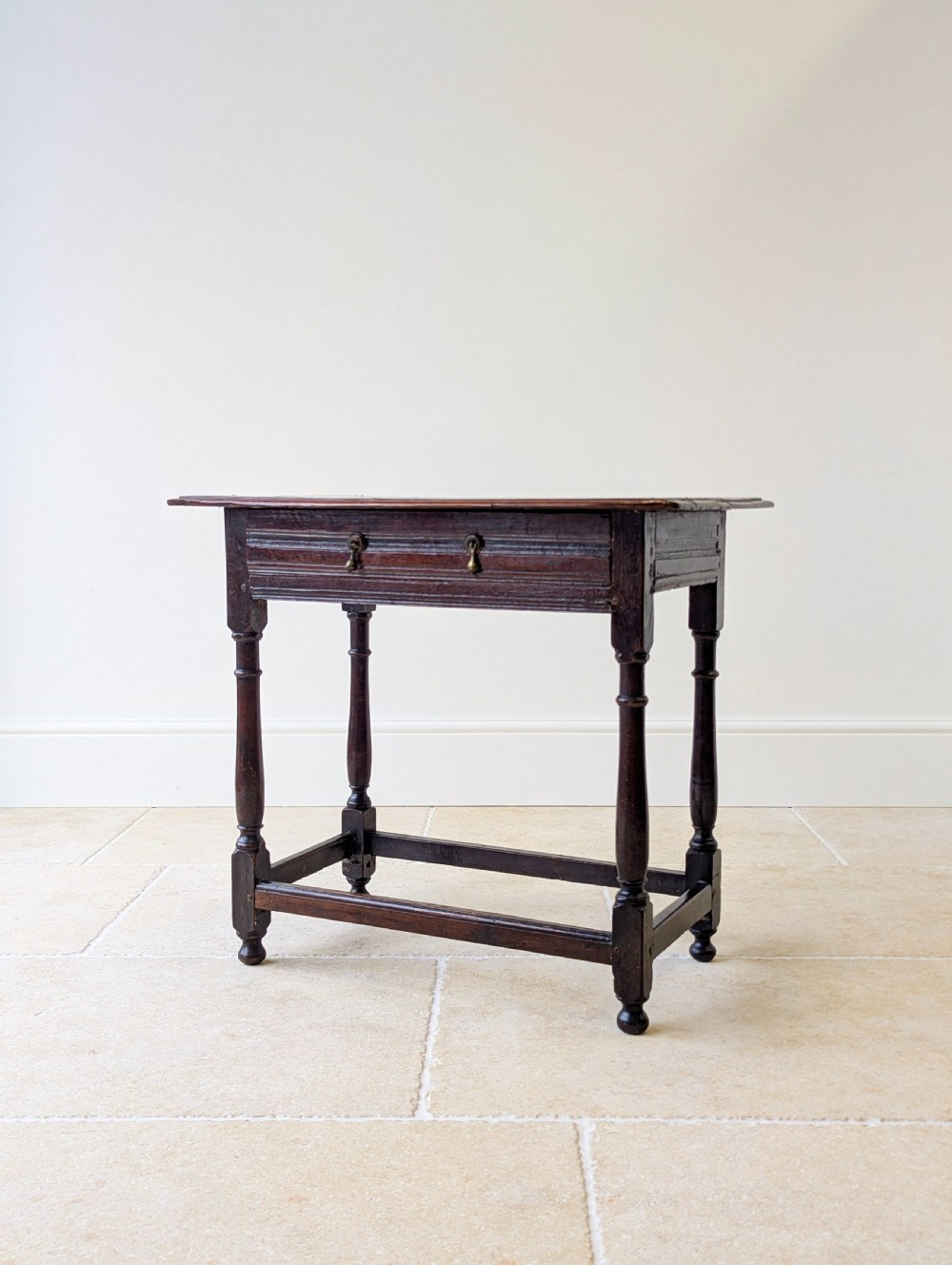 A late 17th-century dark oak side table with turned legs, lower stretchers, and a single drawer featuring brass drop handles. View X