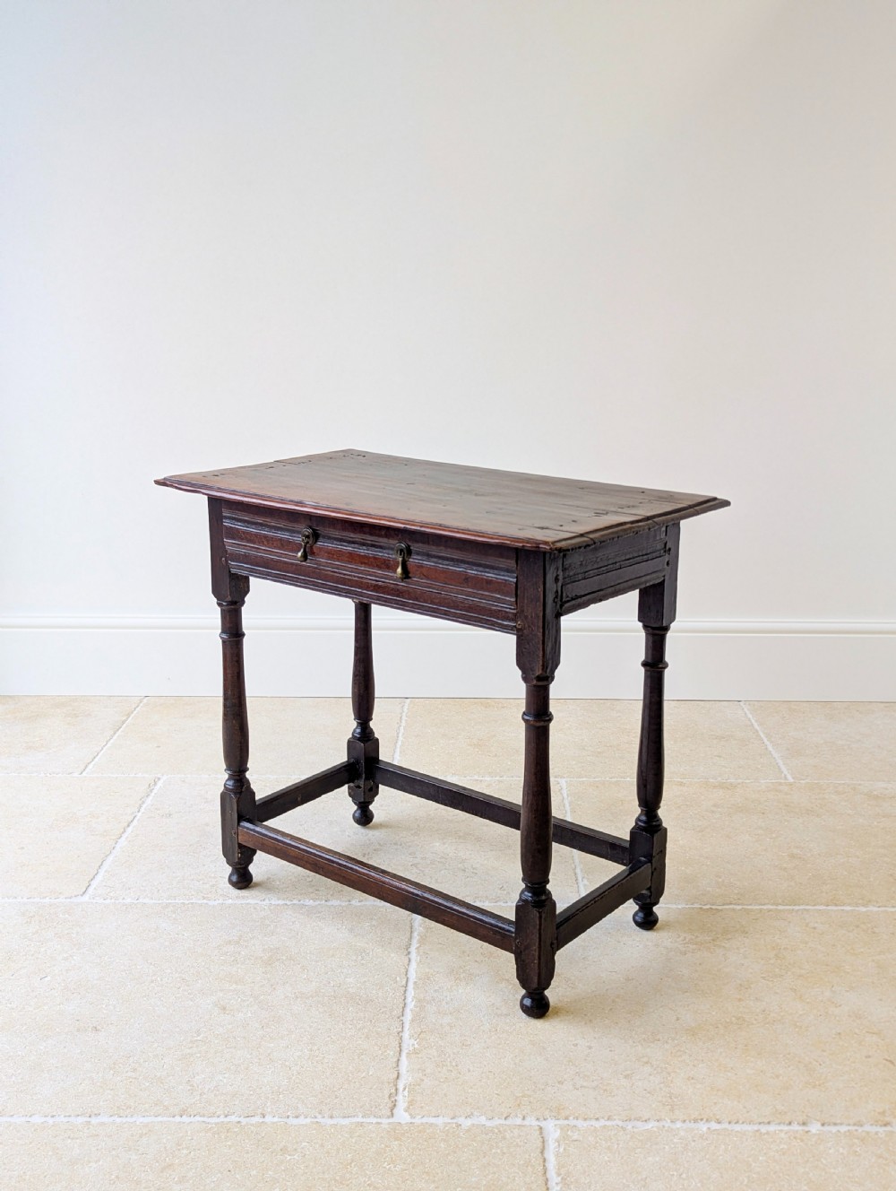 A late 17th-century dark oak side table with turned legs, lower stretchers, and a single drawer featuring brass drop handles. View XVI