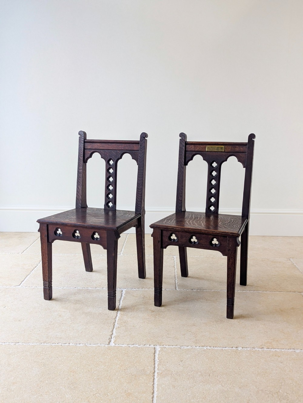 A pair of dark oak Edwardian Gothic Revival side chairs displaying trefoil cutouts, pointed arches, and solid square legs. View X