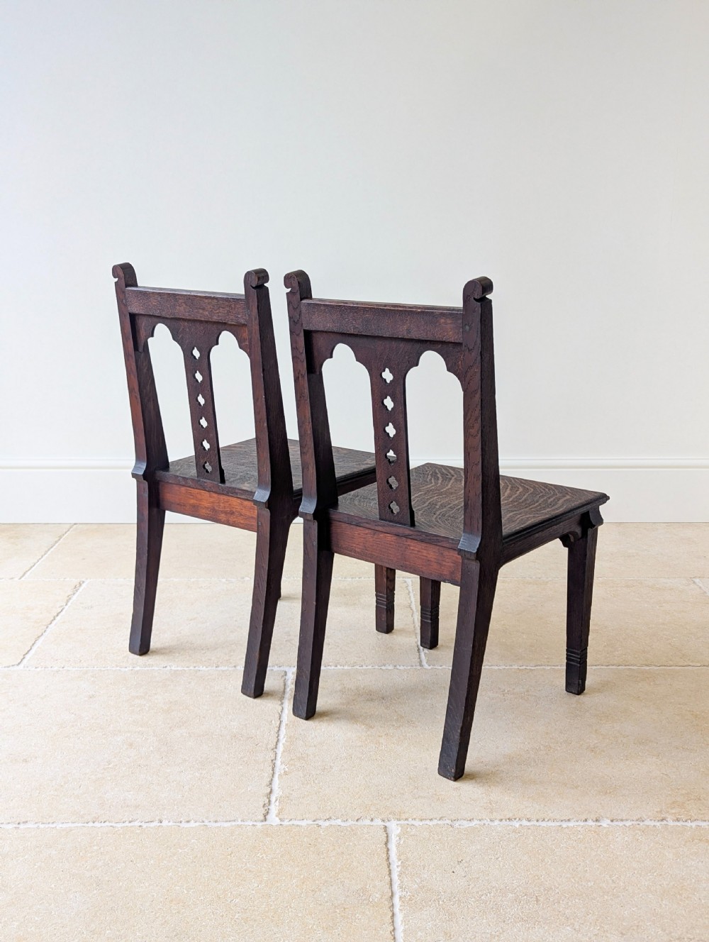 A pair of dark oak Edwardian Gothic Revival side chairs displaying trefoil cutouts, pointed arches, and solid square legs. View XVI