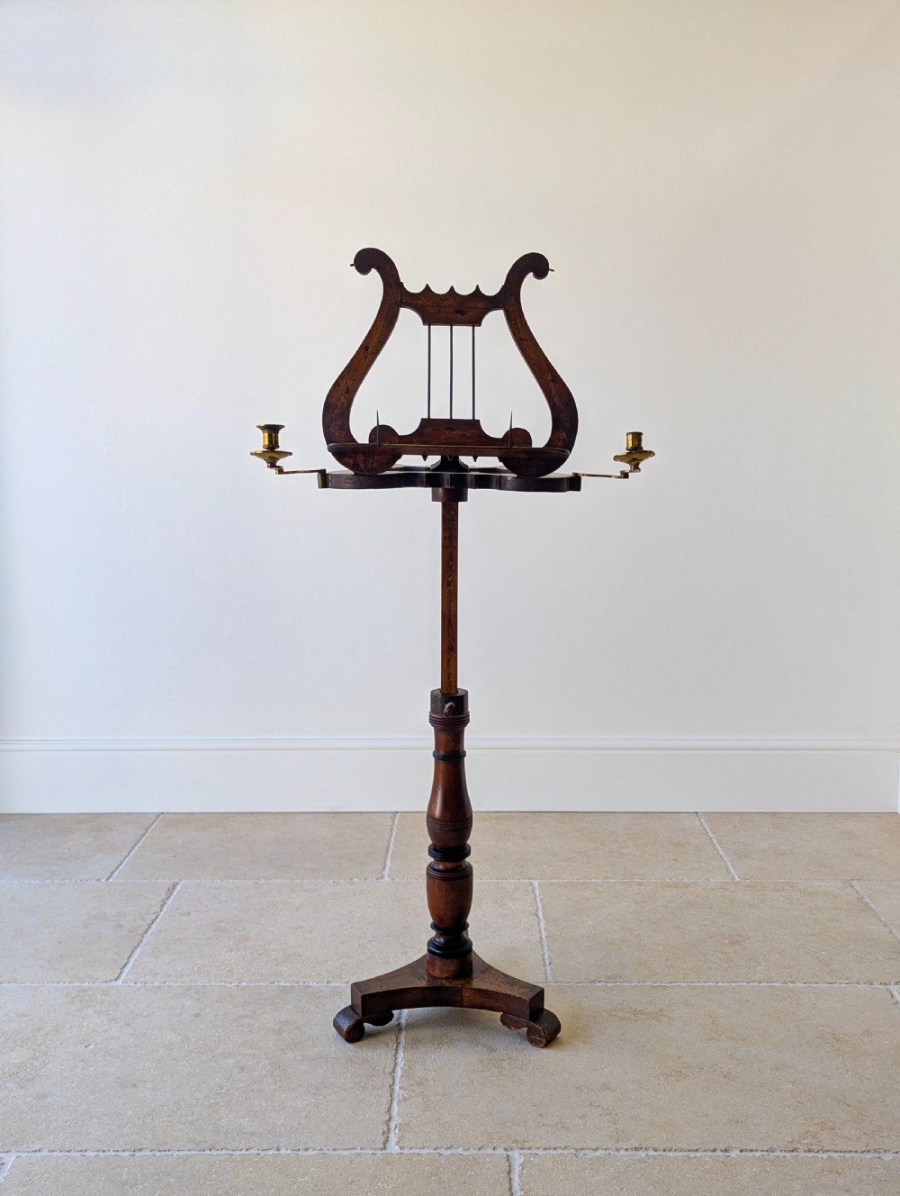 An antique mahogany music stand featuring a lyre-shaped sheet rest, dual brass candle sconces, a turned stem, and a carved tripod base.