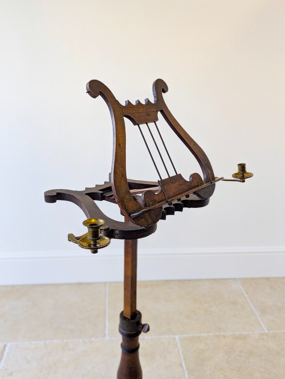 An antique mahogany music stand featuring a lyre-shaped sheet rest, dual brass candle sconces, a turned stem, and a carved tripod base. View II