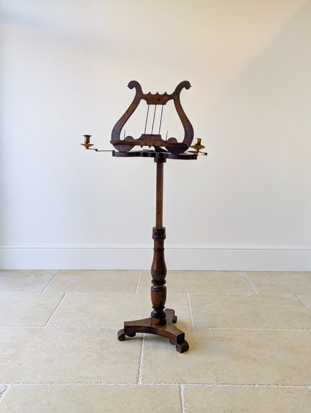 An antique mahogany music stand featuring a lyre-shaped sheet rest, dual brass candle sconces, a turned stem, and a carved tripod base. View III