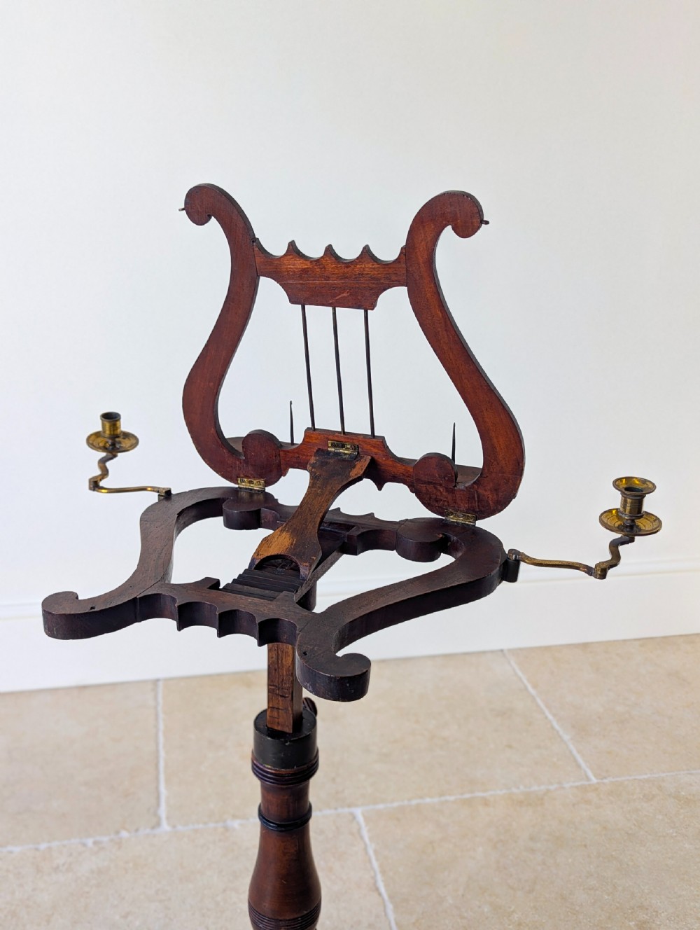 An antique mahogany music stand featuring a lyre-shaped sheet rest, dual brass candle sconces, a turned stem, and a carved tripod base. View IV