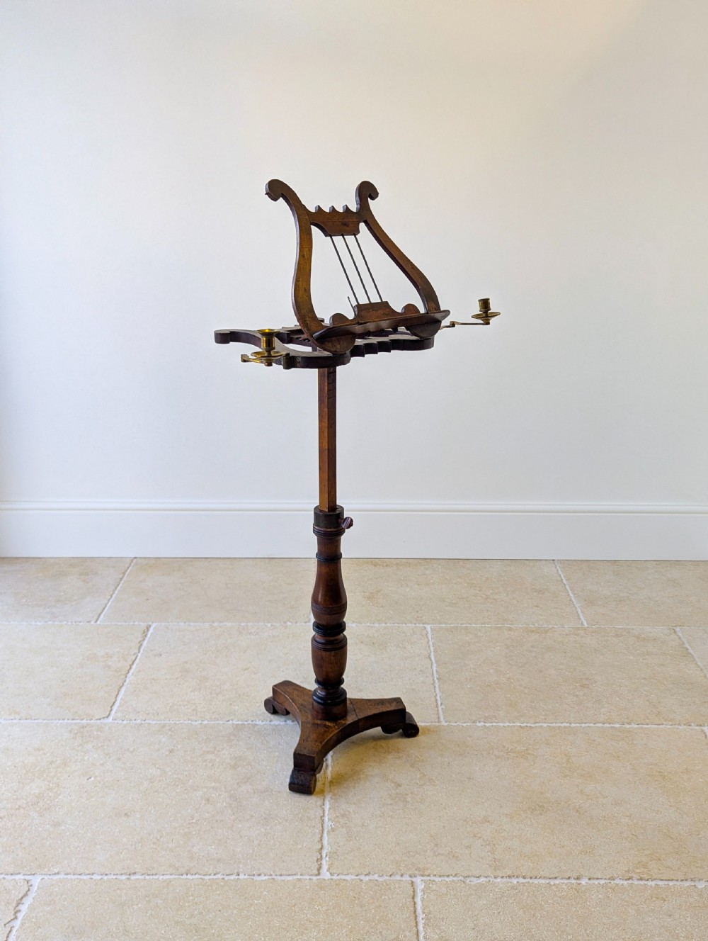 An antique mahogany music stand featuring a lyre-shaped sheet rest, dual brass candle sconces, a turned stem, and a carved tripod base. View VI