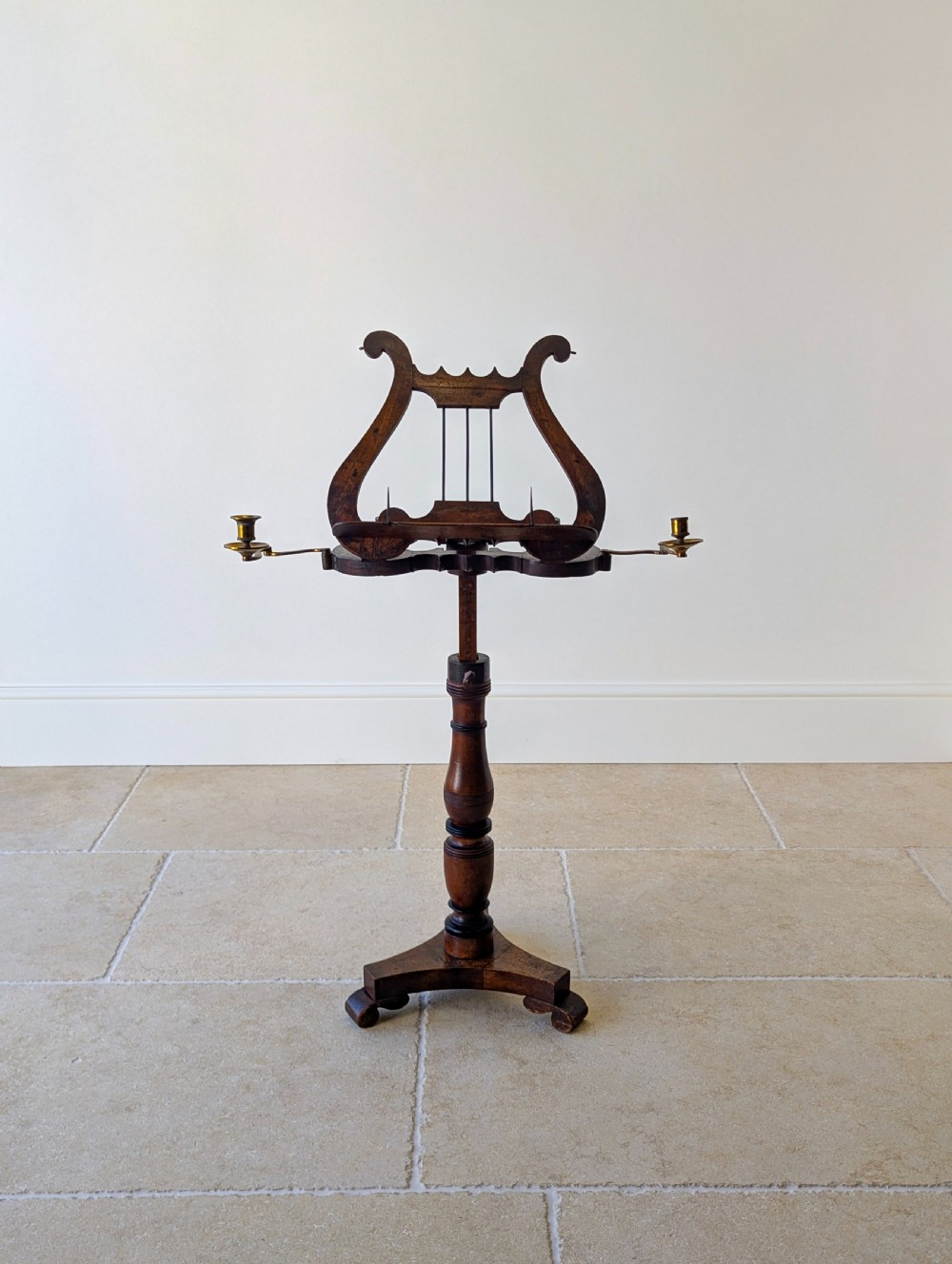 An antique mahogany music stand featuring a lyre-shaped sheet rest, dual brass candle sconces, a turned stem, and a carved tripod base. View XII