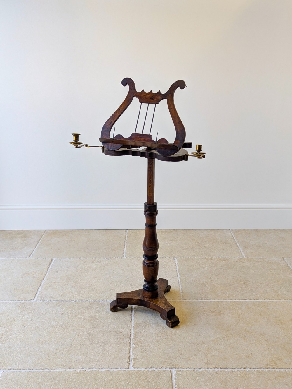 An antique mahogany music stand featuring a lyre-shaped sheet rest, dual brass candle sconces, a turned stem, and a carved tripod base. View XV