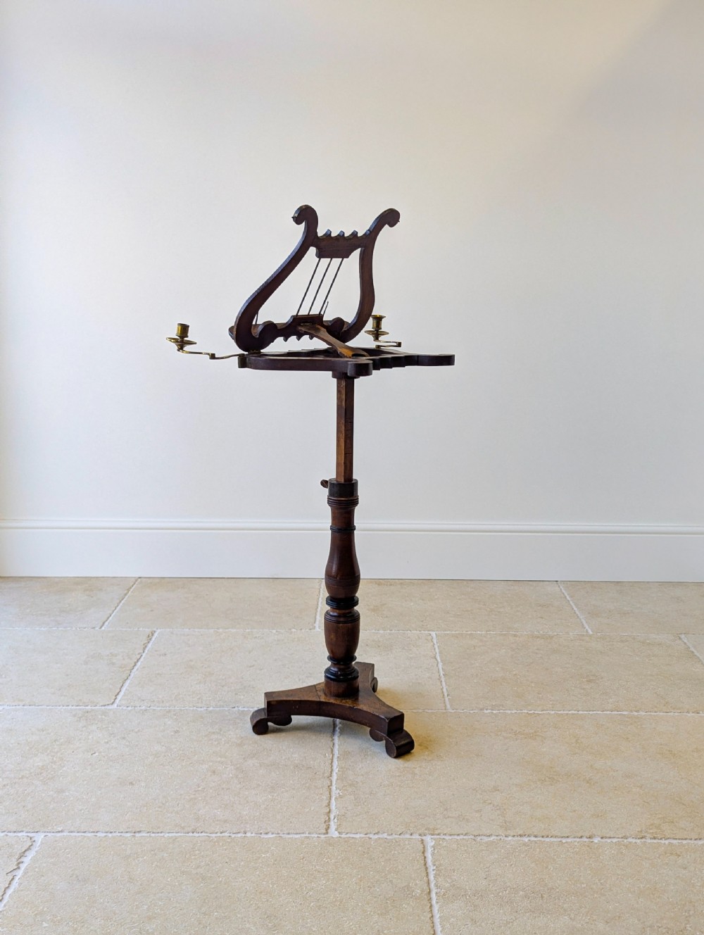 An antique mahogany music stand featuring a lyre-shaped sheet rest, dual brass candle sconces, a turned stem, and a carved tripod base. View XVII
