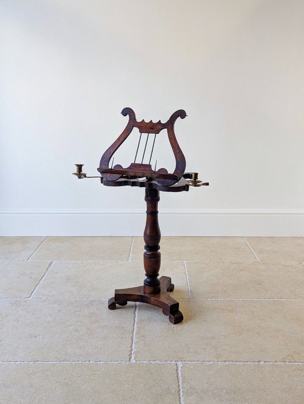 An antique mahogany music stand featuring a lyre-shaped sheet rest, dual brass candle sconces, a turned stem, and a carved tripod base. View XIX