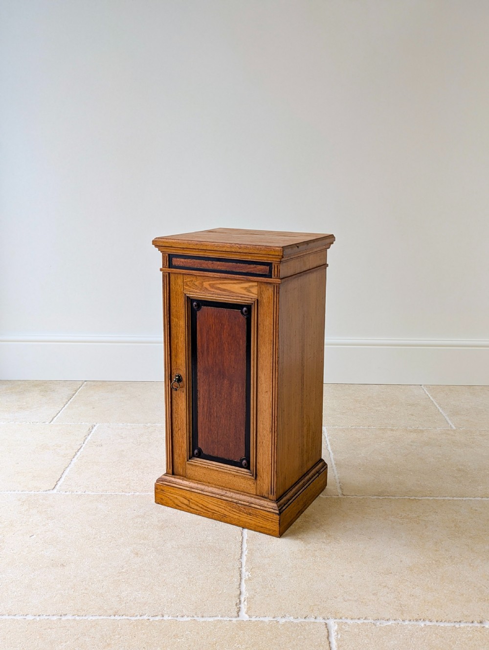 A late Victorian Aesthetic Movement oak bedside cabinet featuring an ebonised inset panel door and drop ring handle.