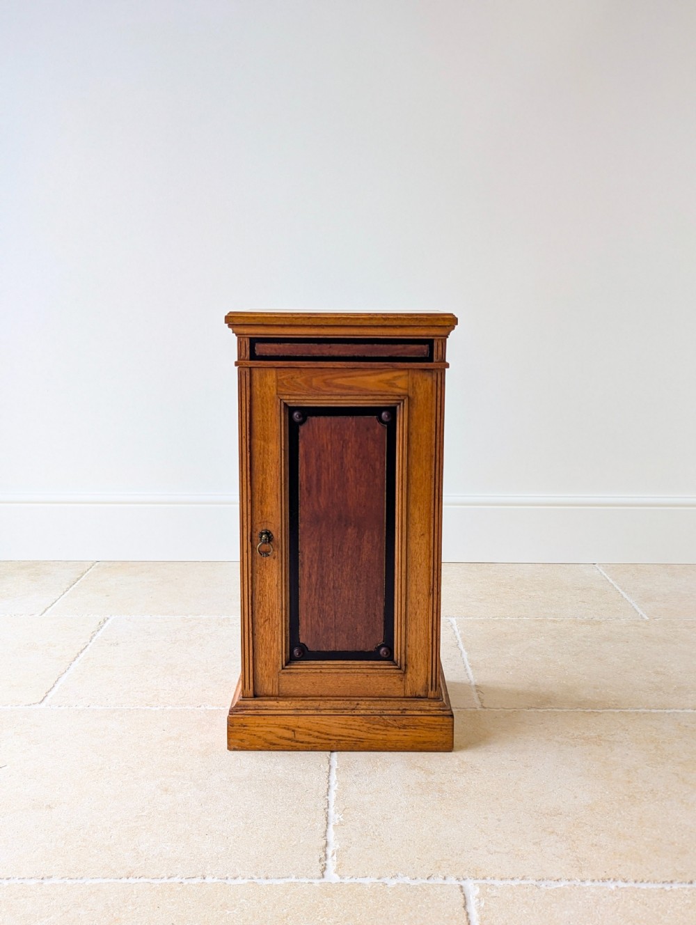 A late Victorian Aesthetic Movement oak bedside cabinet featuring an ebonised inset panel door and drop ring handle. View III