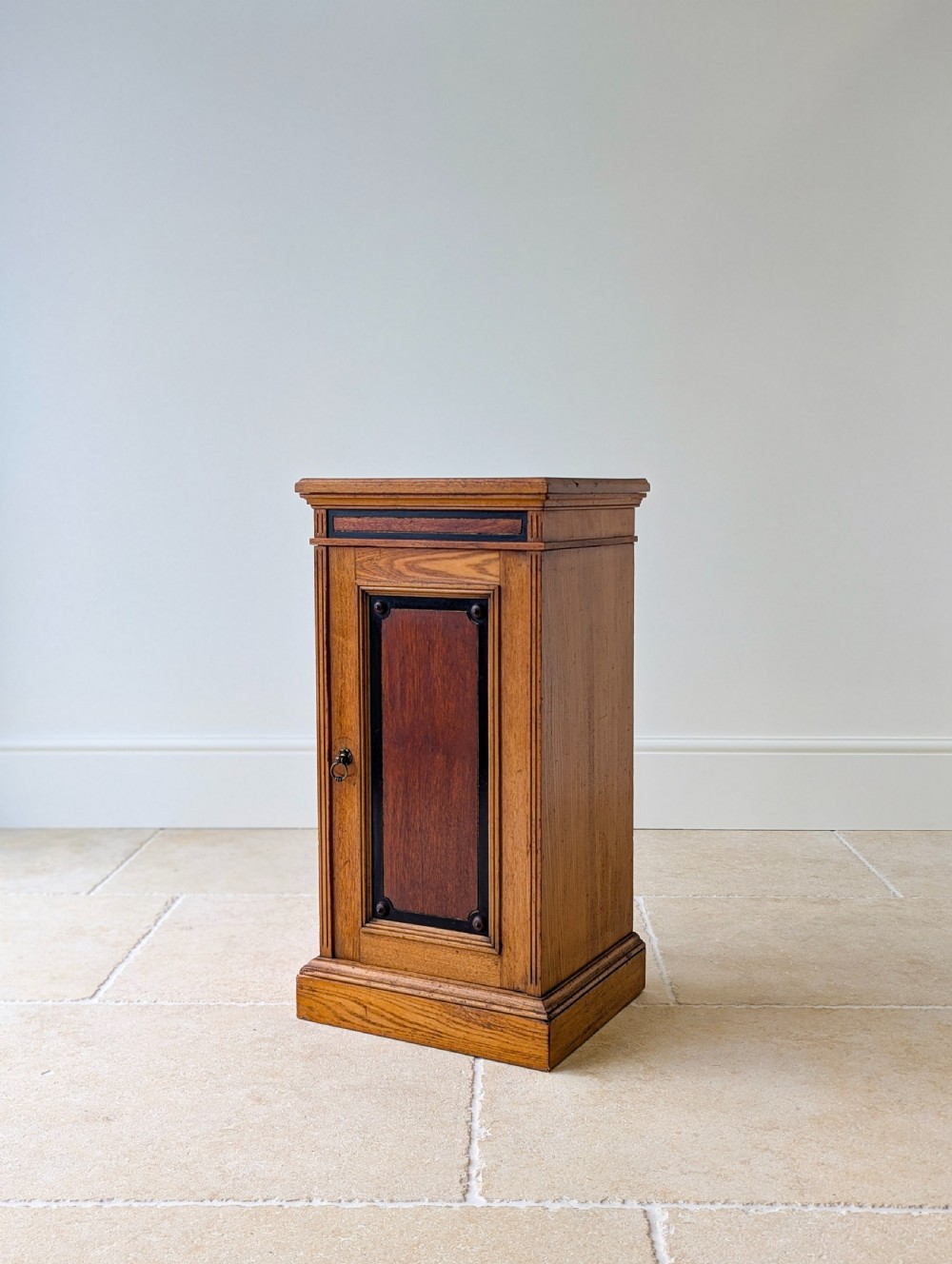 A late Victorian Aesthetic Movement oak bedside cabinet featuring an ebonised inset panel door and drop ring handle. View V