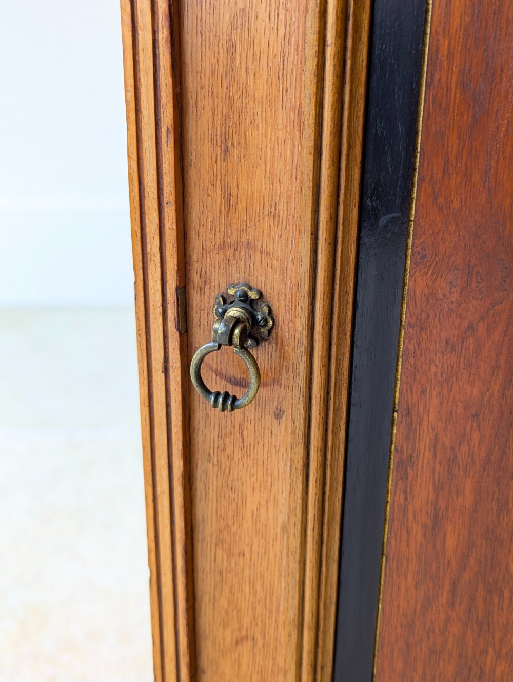 A late Victorian Aesthetic Movement oak bedside cabinet featuring an ebonised inset panel door and drop ring handle. View VI