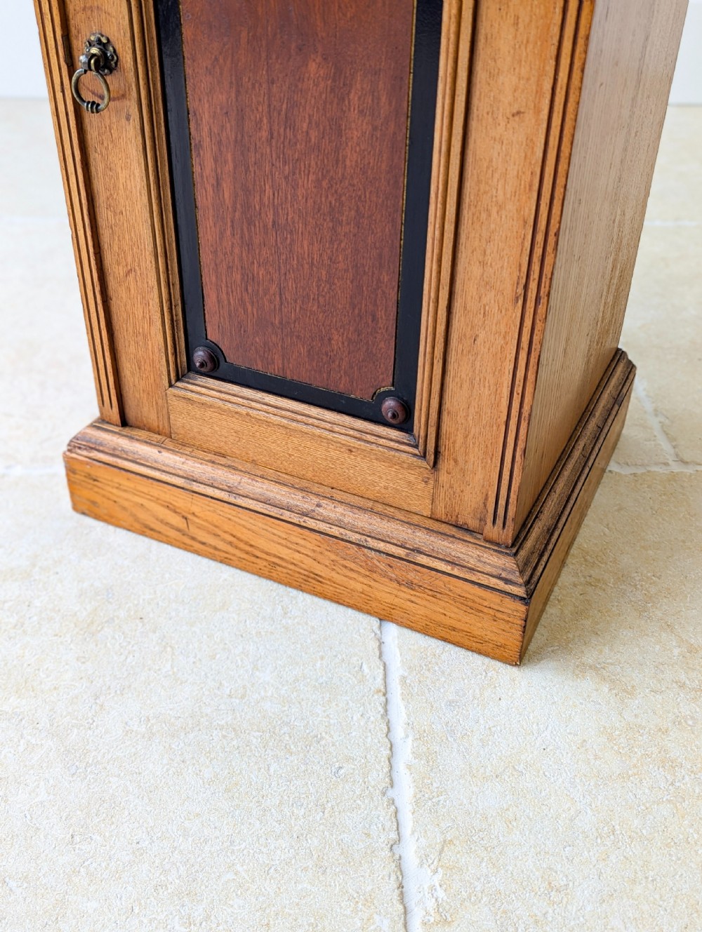 A late Victorian Aesthetic Movement oak bedside cabinet featuring an ebonised inset panel door and drop ring handle. View X