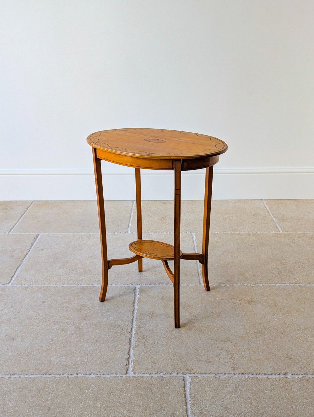 An Edwardian oval satinwood occasional table featuring delicate marquetry inlay on the top, slender splayed legs, and a small oval undertier.