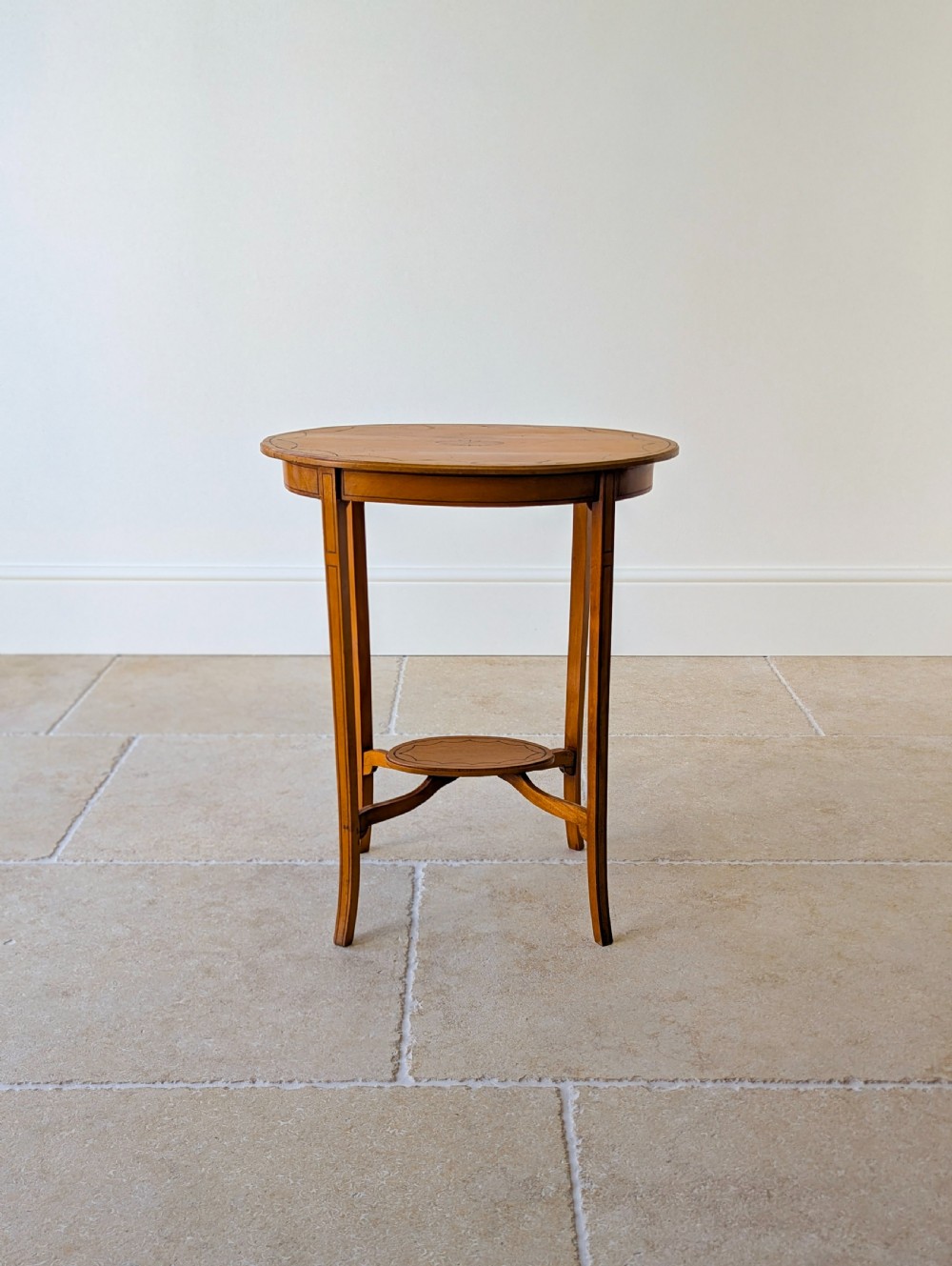 An Edwardian oval satinwood occasional table featuring delicate marquetry inlay on the top, slender splayed legs, and a small oval undertier. View II
