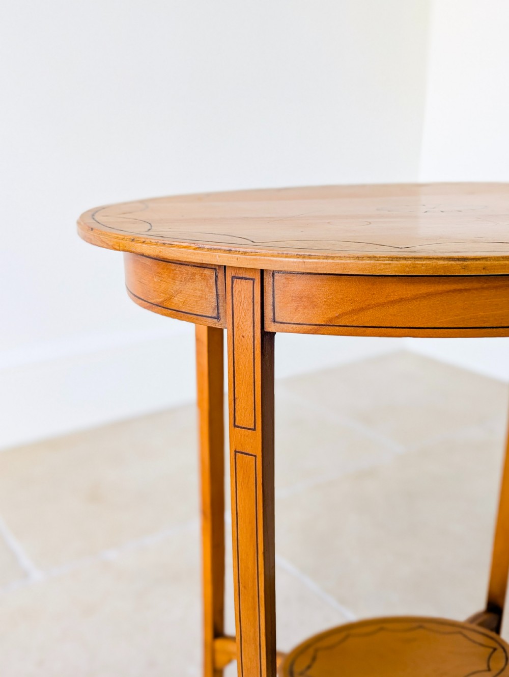 An Edwardian oval satinwood occasional table featuring delicate marquetry inlay on the top, slender splayed legs, and a small oval undertier. View V