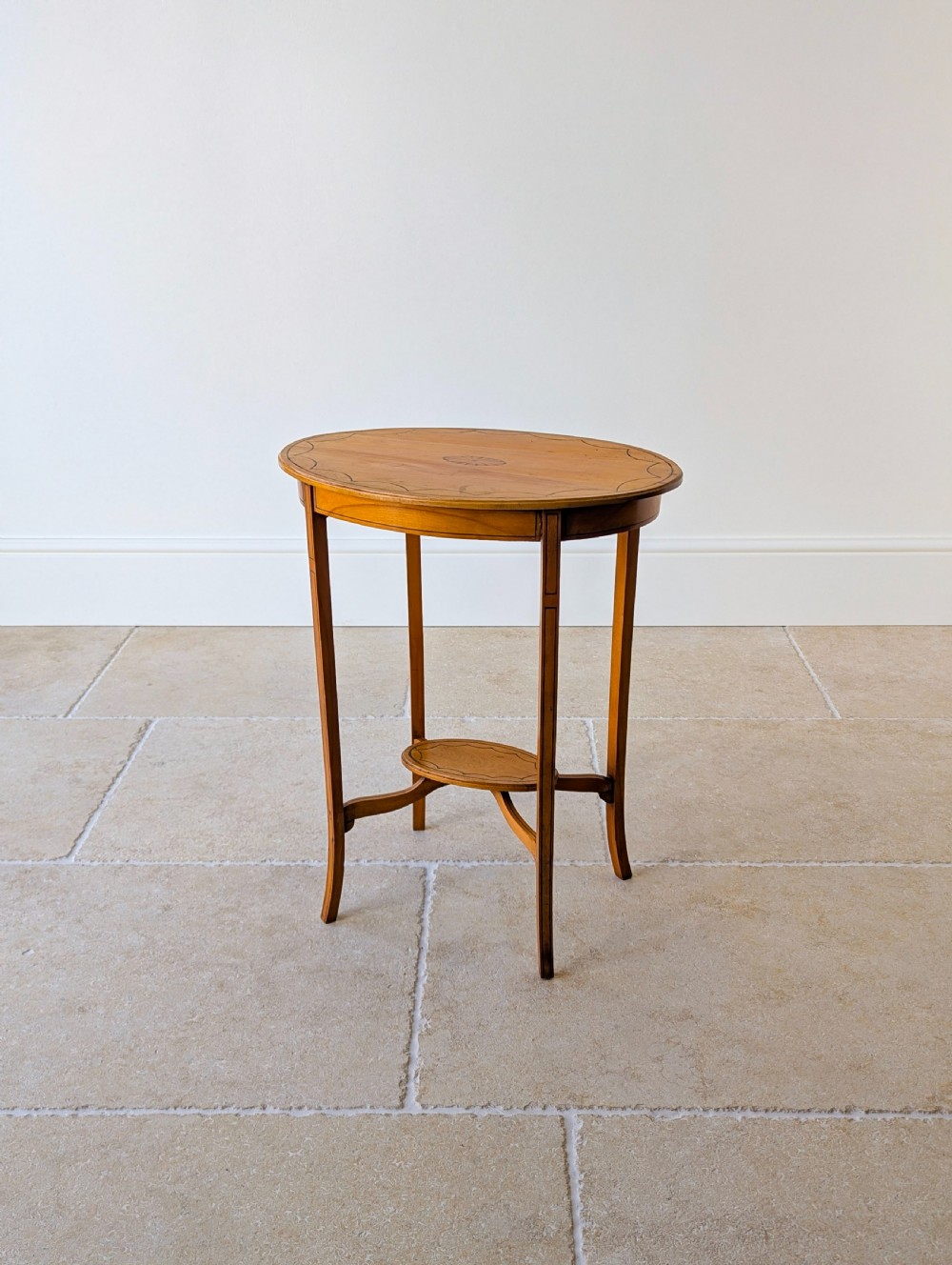 An Edwardian oval satinwood occasional table featuring delicate marquetry inlay on the top, slender splayed legs, and a small oval undertier. View VIII