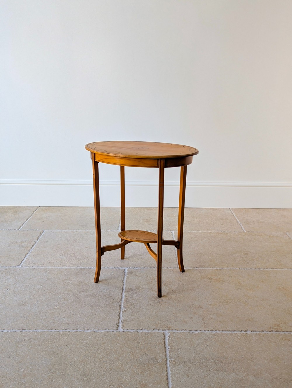 An Edwardian oval satinwood occasional table featuring delicate marquetry inlay on the top, slender splayed legs, and a small oval undertier. View XI