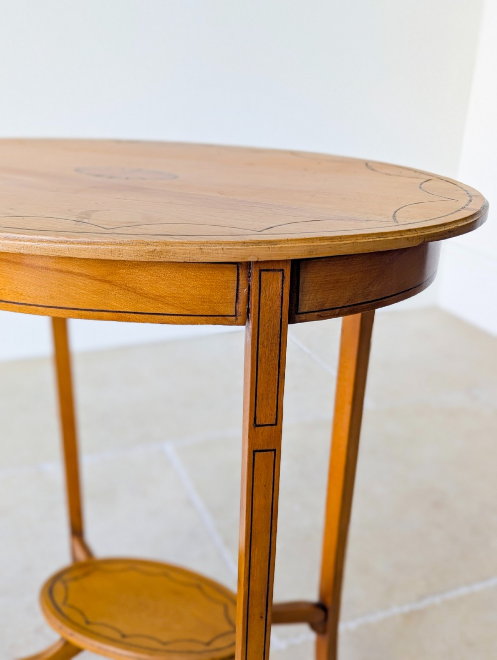 An Edwardian oval satinwood occasional table featuring delicate marquetry inlay on the top, slender splayed legs, and a small oval undertier. View XIV