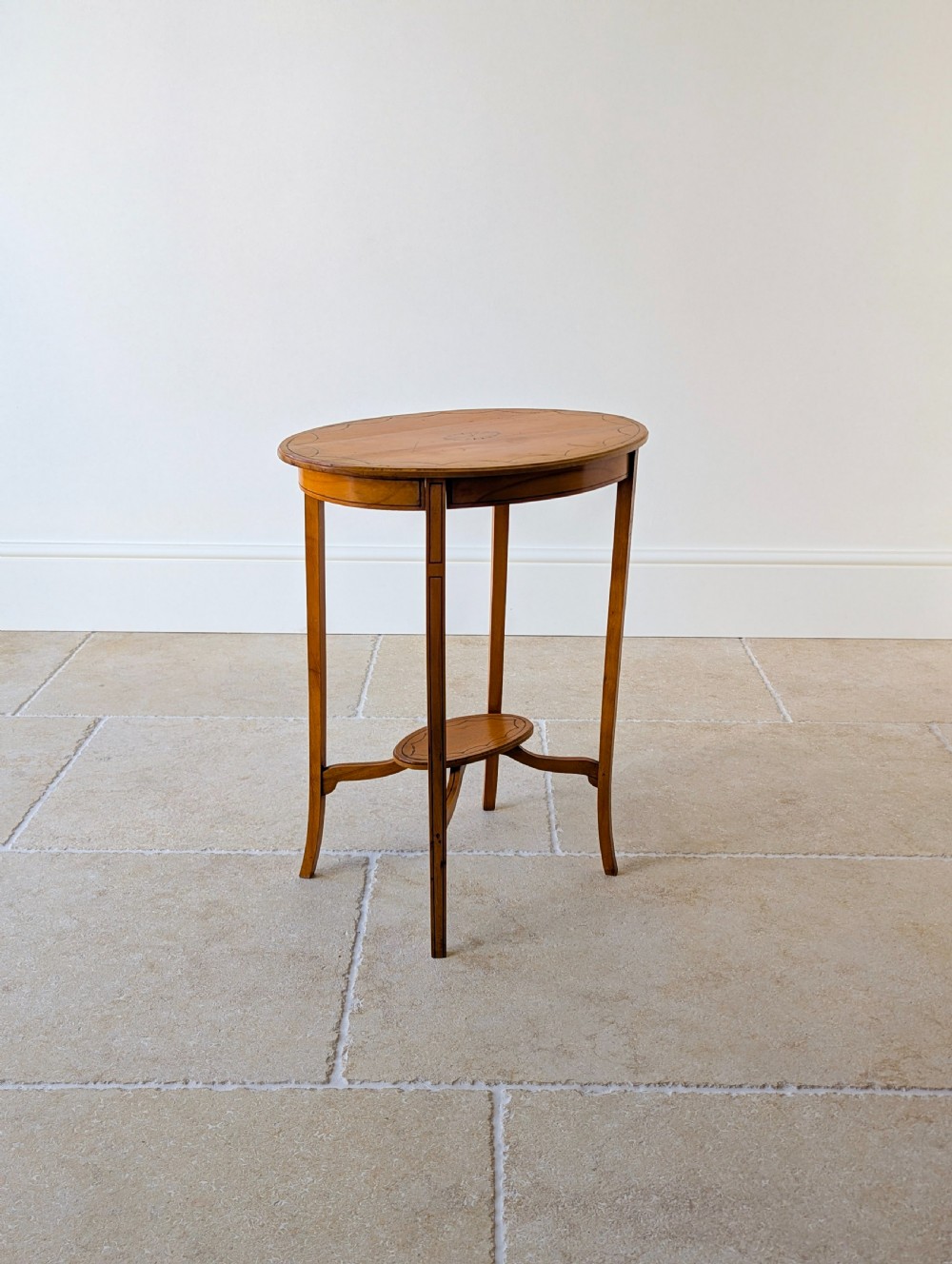 An Edwardian oval satinwood occasional table featuring delicate marquetry inlay on the top, slender splayed legs, and a small oval undertier. View XV