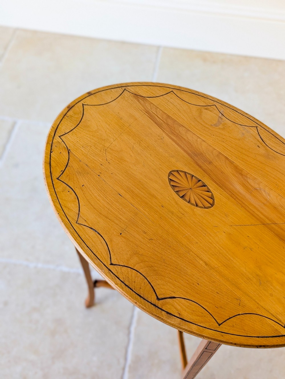 An Edwardian oval satinwood occasional table featuring delicate marquetry inlay on the top, slender splayed legs, and a small oval undertier. View XVIII