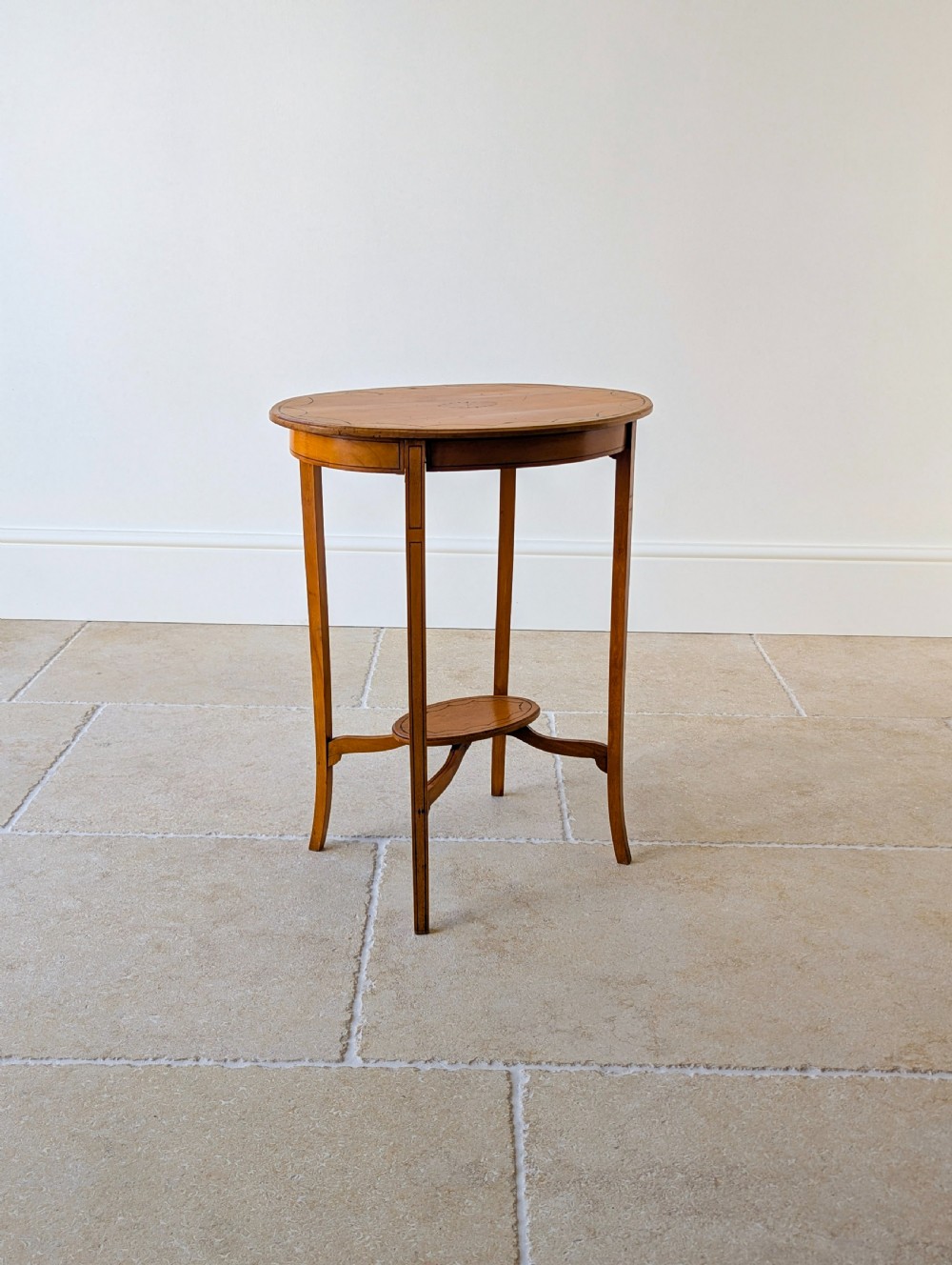 An Edwardian oval satinwood occasional table featuring delicate marquetry inlay on the top, slender splayed legs, and a small oval undertier. View XIX
