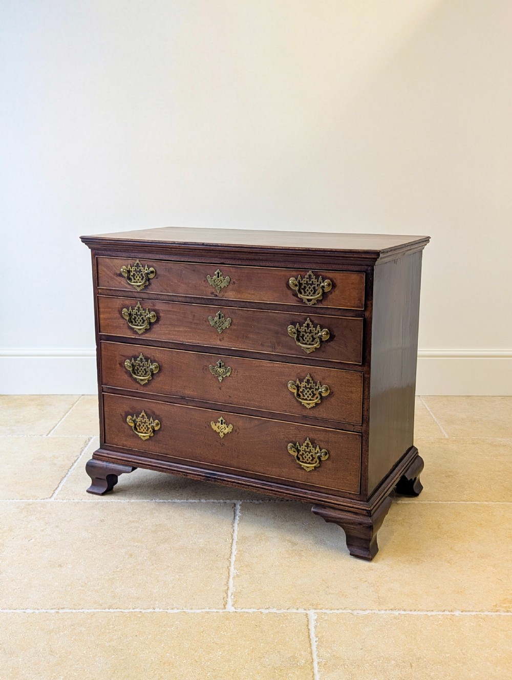 An antique George II mahogany chest of drawers featuring four graduated drawers with ornate brass handles on bracket feet.