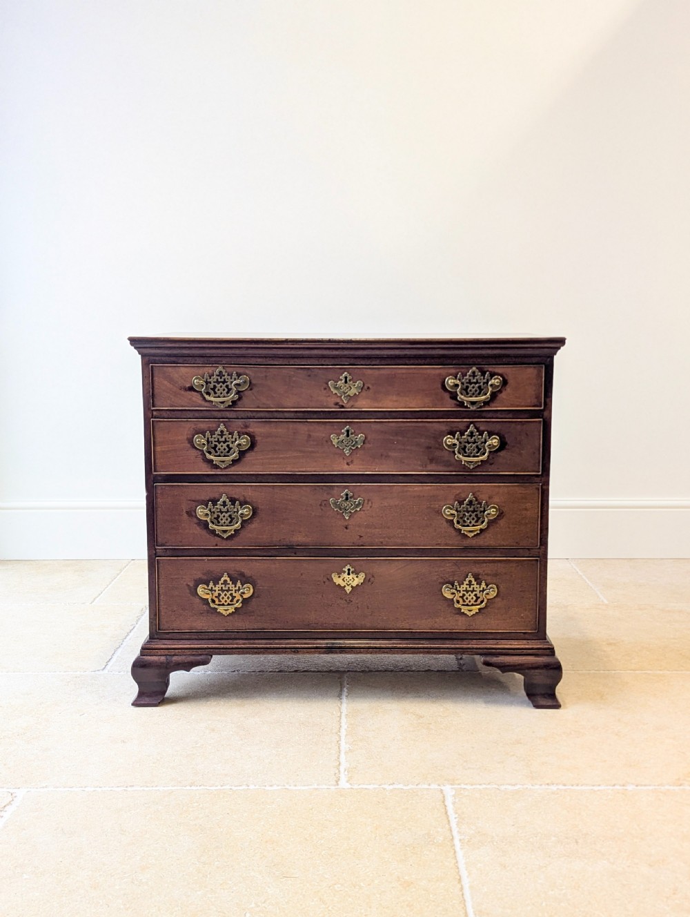 An antique George II mahogany chest of drawers featuring four graduated drawers with ornate brass handles on bracket feet. View II
