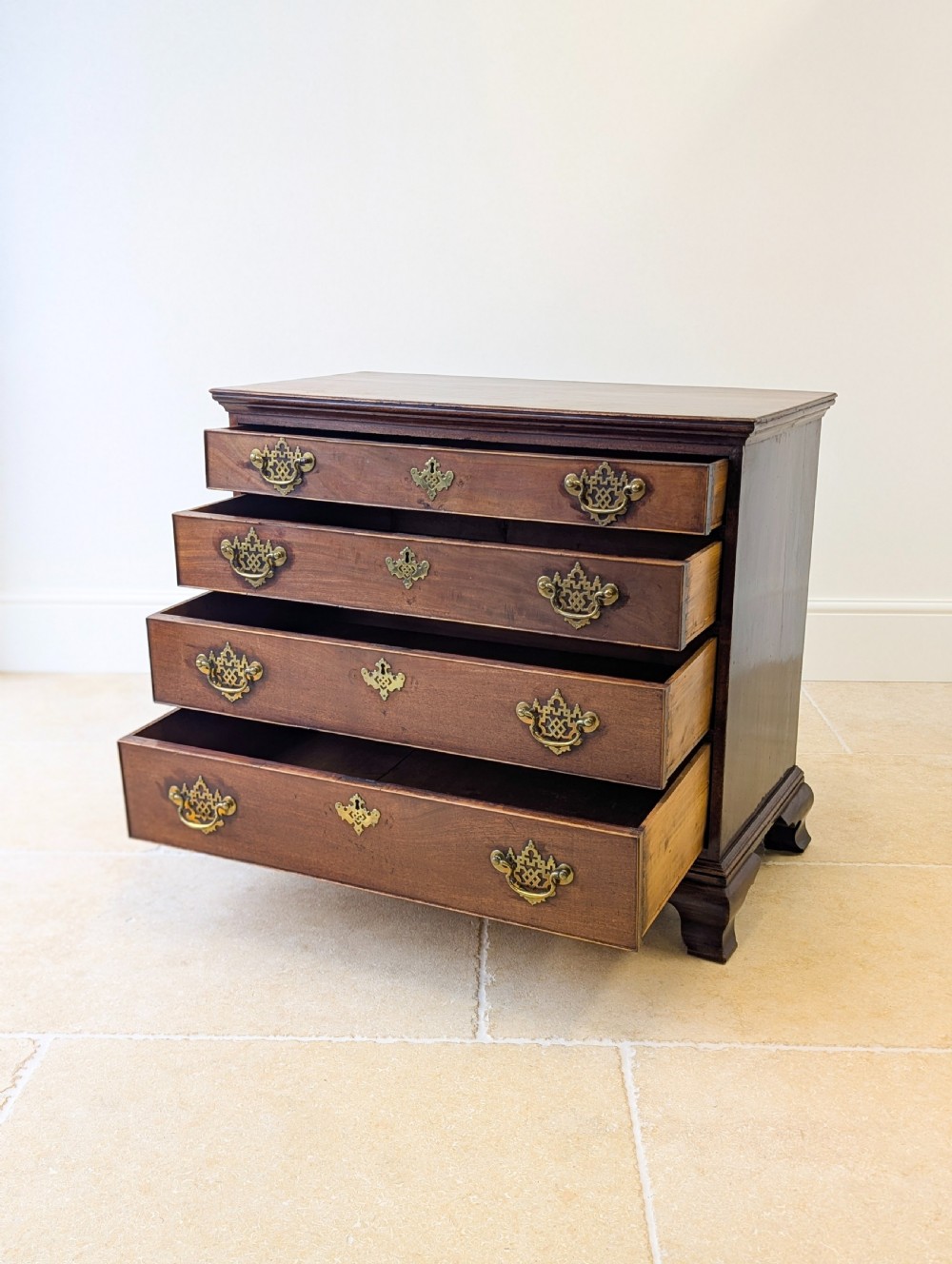 An antique George II mahogany chest of drawers featuring four graduated drawers with ornate brass handles on bracket feet. View IV