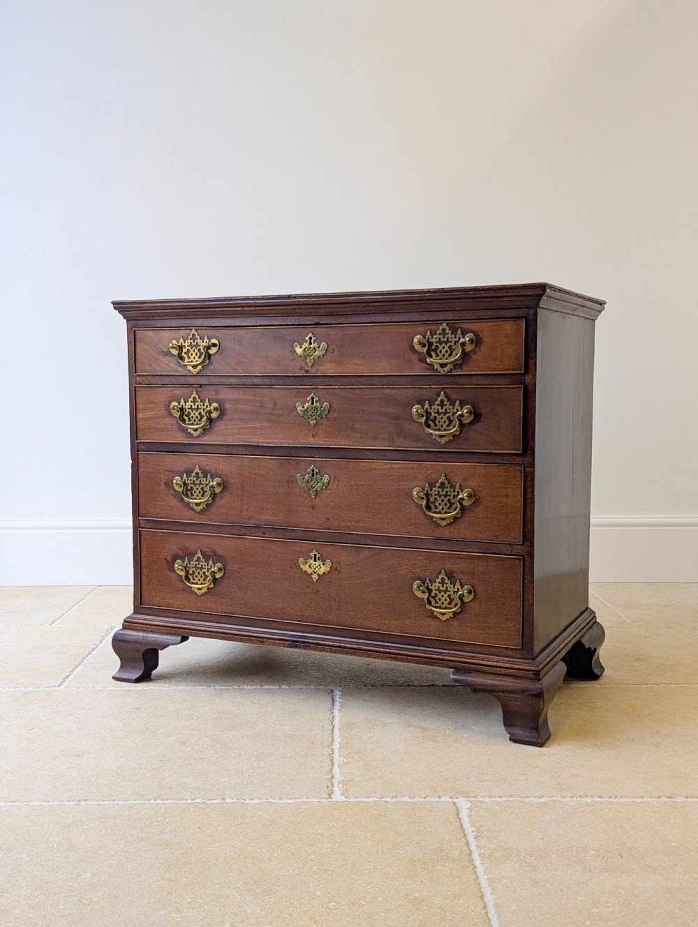An antique George II mahogany chest of drawers featuring four graduated drawers with ornate brass handles on bracket feet. View V