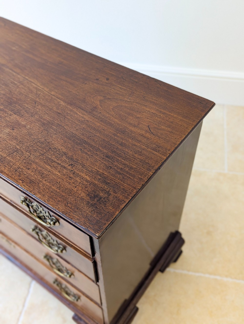 An antique George II mahogany chest of drawers featuring four graduated drawers with ornate brass handles on bracket feet. View X