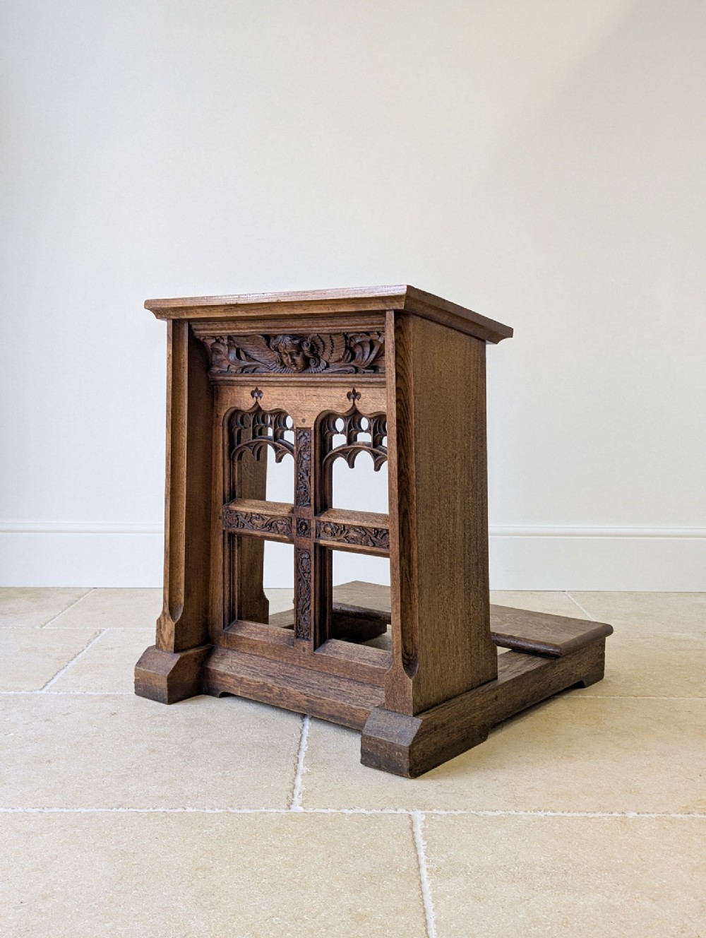 A Victorian Gothic Revival oak prie-dieu featuring carved tracery arches, a central cross motif, a cherub frieze, and a low kneeling step.