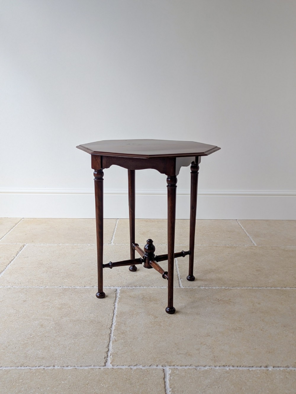 An antique dark mahogany occasional table featuring an octagonal top, turned slender legs, shaped aprons, and a central finial on a cross stretcher.