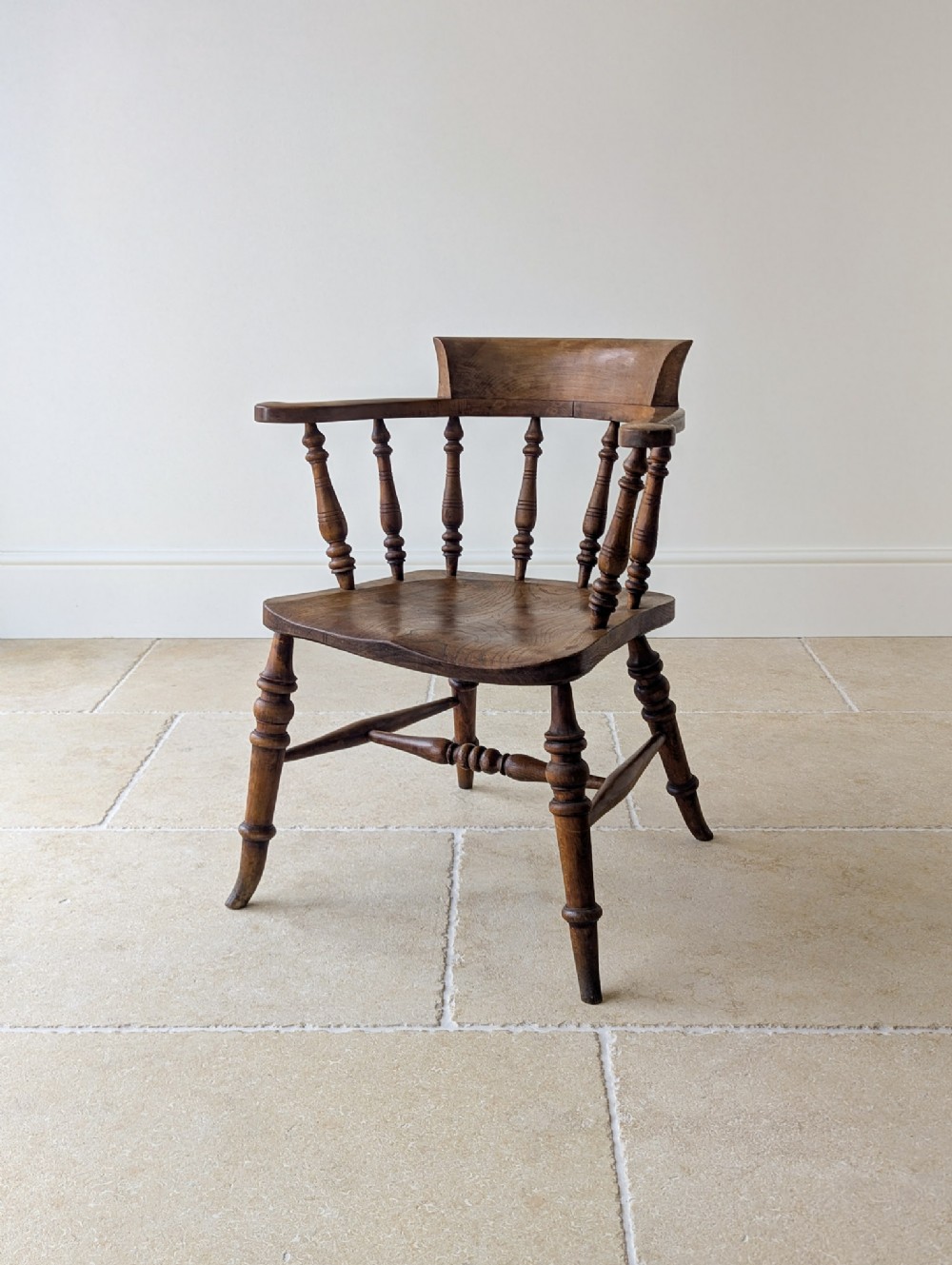 A Victorian elm and beech captains desk chair featuring a curved backrail, turned spindles, a contoured saddle seat, and turned legs with a stretcher base.