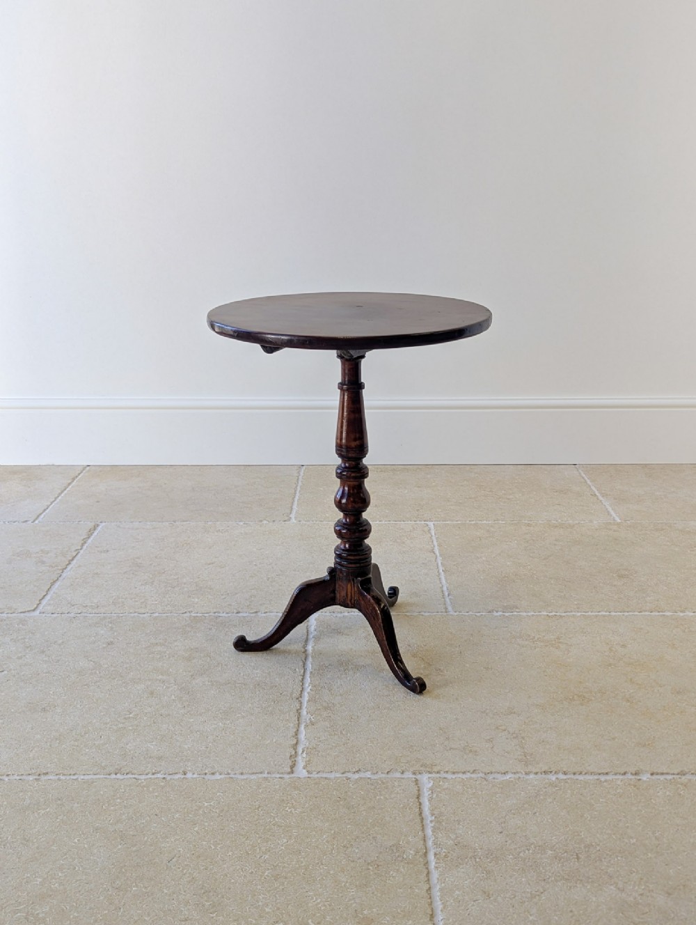 An 18th-century George III mahogany tilt-top table featuring a circular top, a baluster turned column, and three shaped tripod legs.