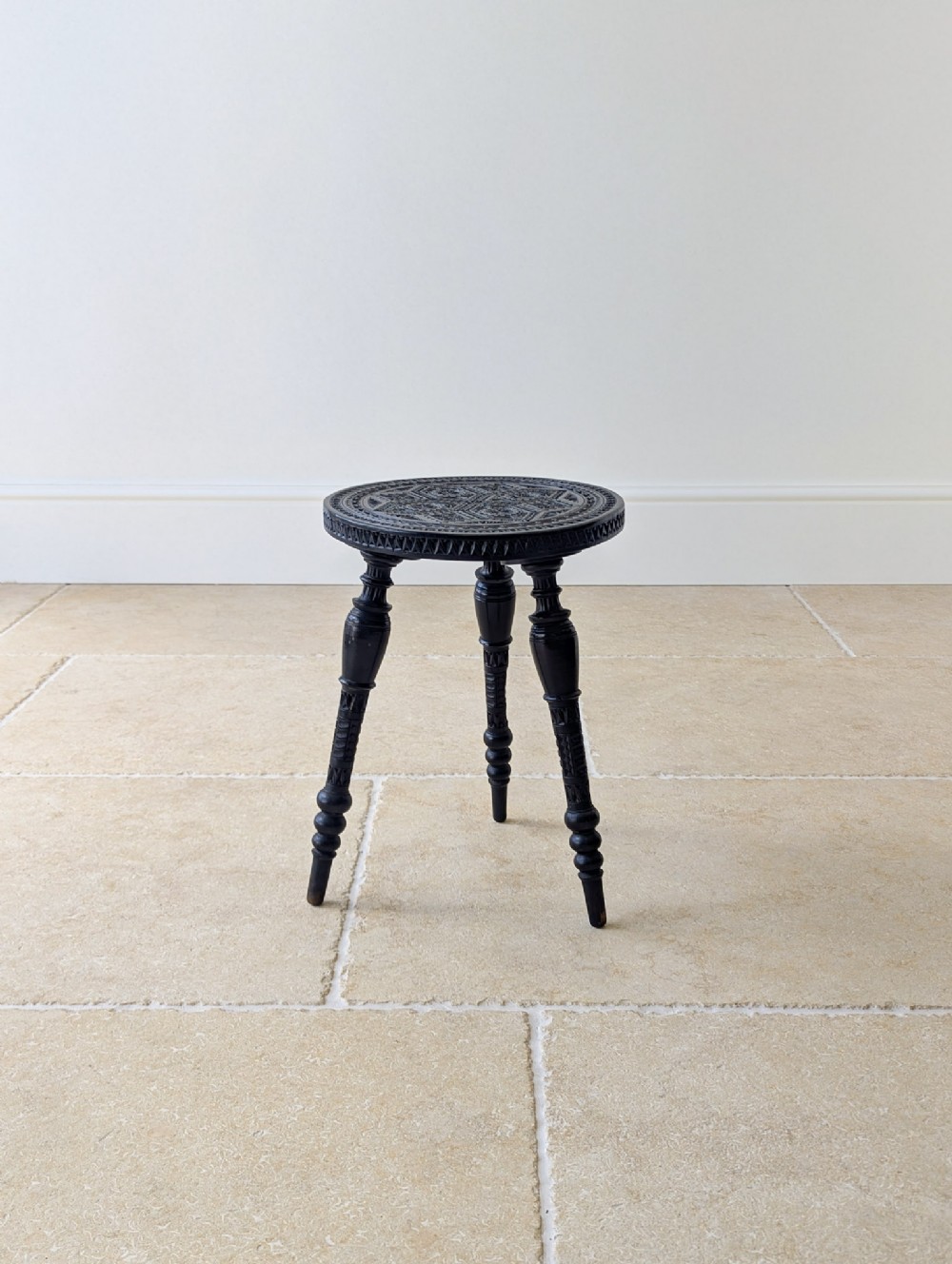 A small round Victorian ebonised wooden occasional table with detailed geometric chip carving on the top and three turned legs.