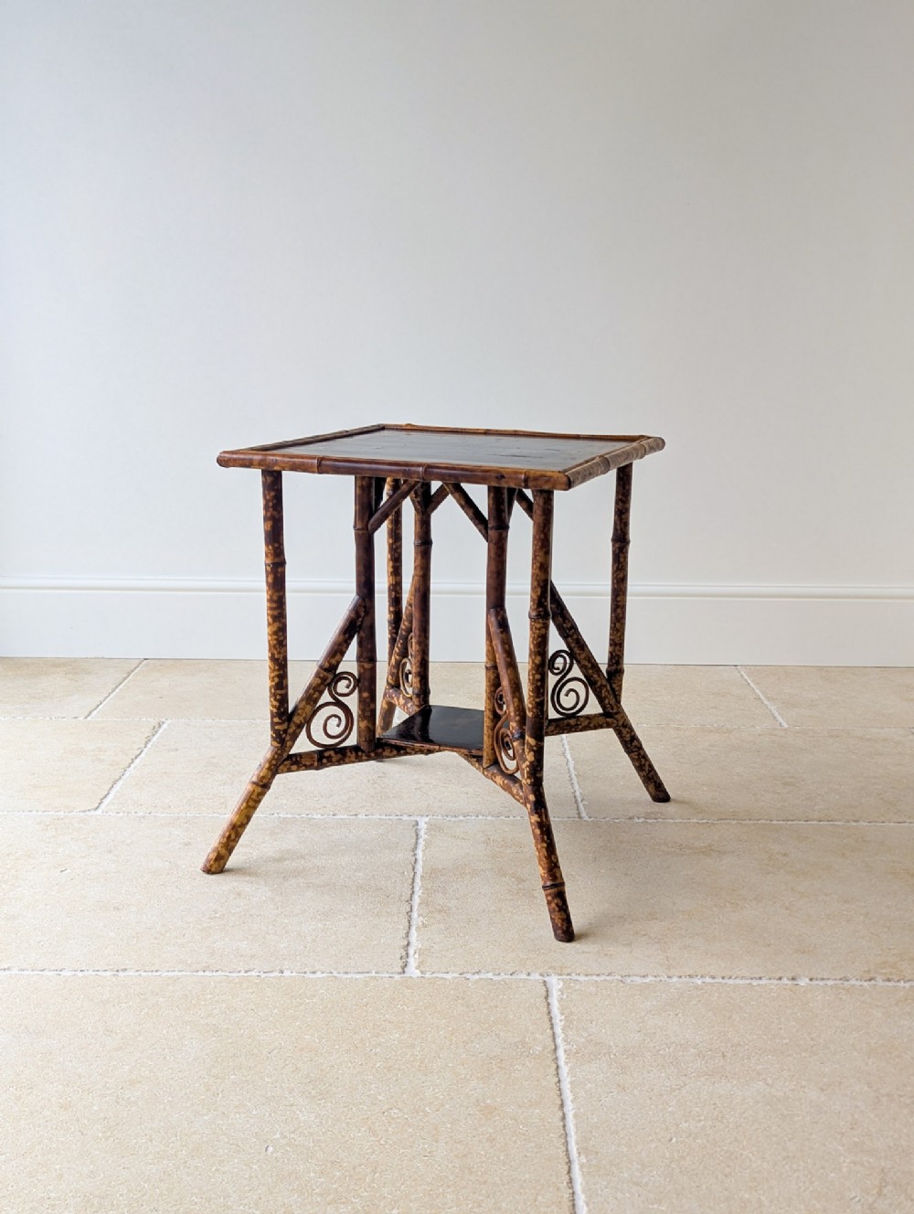 A late 19th-century bamboo occasional table featuring a dark lacquered square top, tortoiseshell bamboo frame, decorative side scrollwork, and a lower square undertier.