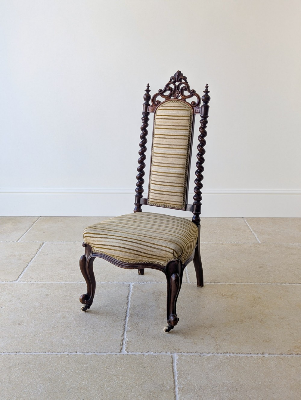 A Mid-Victorian walnut high-back parlour chair featuring barley twist uprights, carved cresting, striped upholstery, and cabriole front legs with castors.