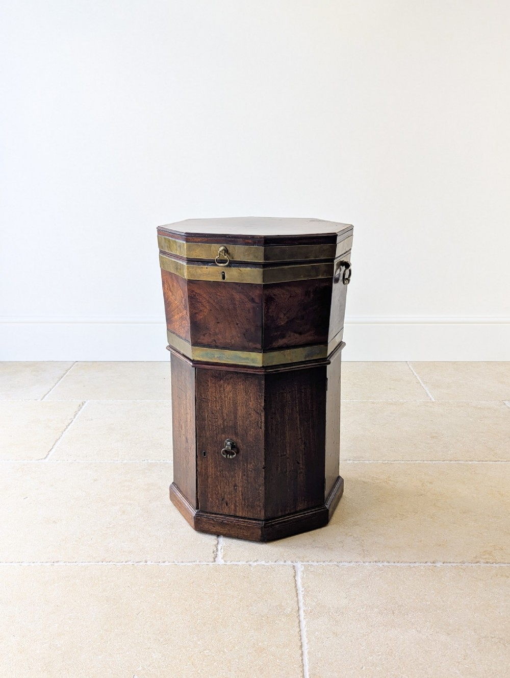 An octagonal dark mahogany George III cellaret with brass binding bands, side handles, and a lower enclosure.
