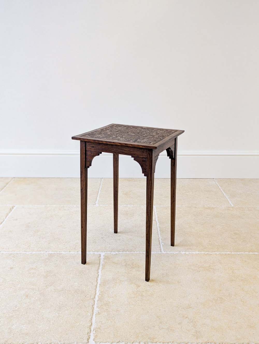 An Edwardian dark oak occasional table featuring a relief-carved square top, shaped corner brackets, and four straight tapered legs.