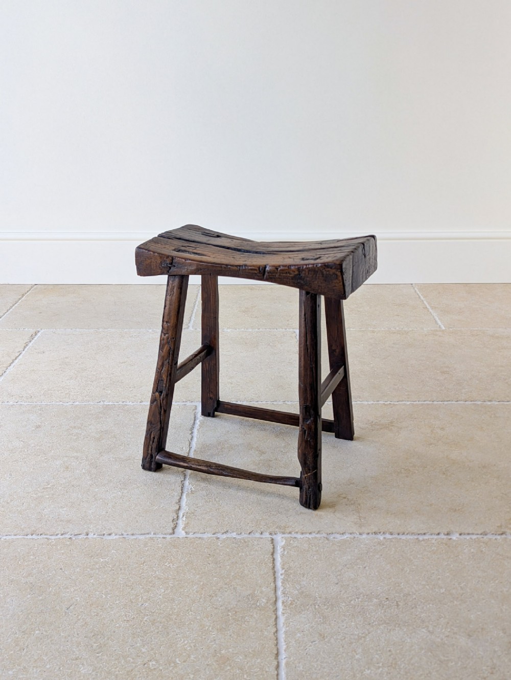A dark oak 18th-century stool featuring a concave dished seat, splayed legs, and rustic wooden stretchers.