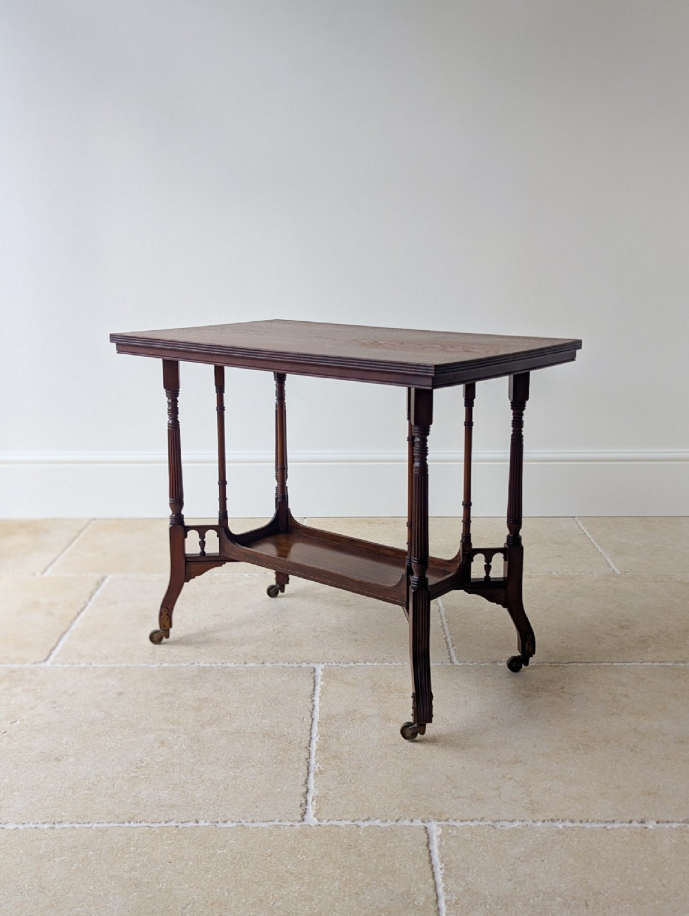 A dark mahogany rectangular side table featuring fluted turned legs, a lower shelf tier, and brass castors.