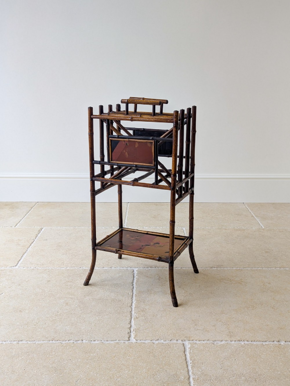 Victorian Aesthetic Movement dark brown bamboo canterbury with vertical compartments, lacquered decorative panels, and a lower open shelf.
