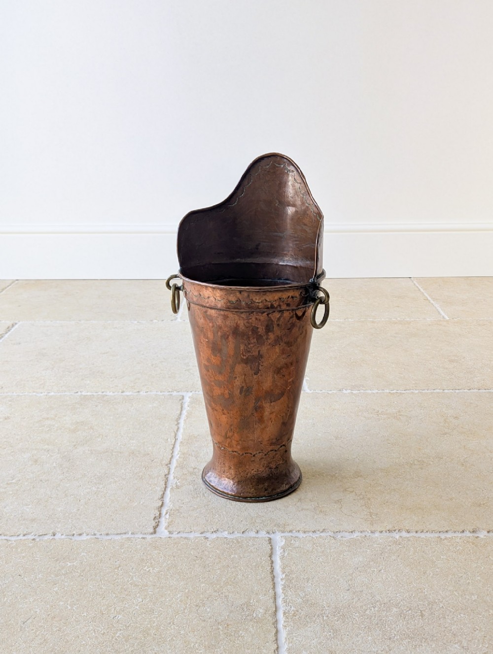 A tall, hand-hammered French copper grape hod featuring a raised back rim, brass ring handles, and a flared base.