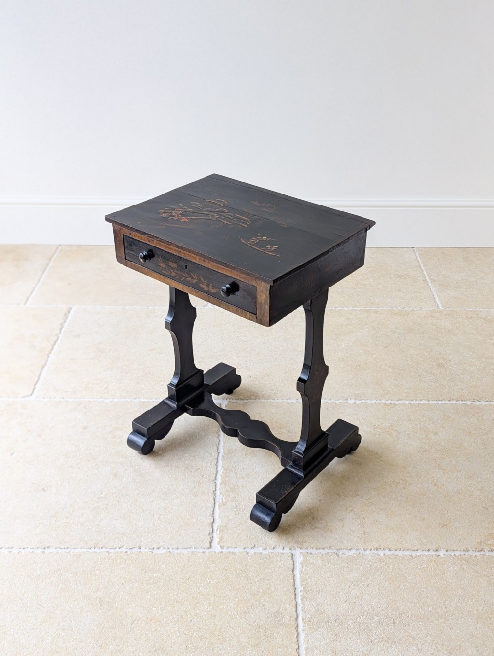 An antique Regency ebonised work table featuring Chinoiserie artwork on the rectangular top, a single drawer, and trestle support legs.