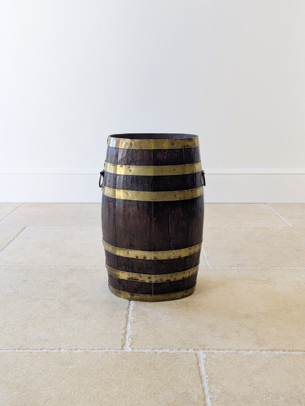 A cylindrical coopered dark oak stick stand bound with polished brass bands and fitted with side drop handles.