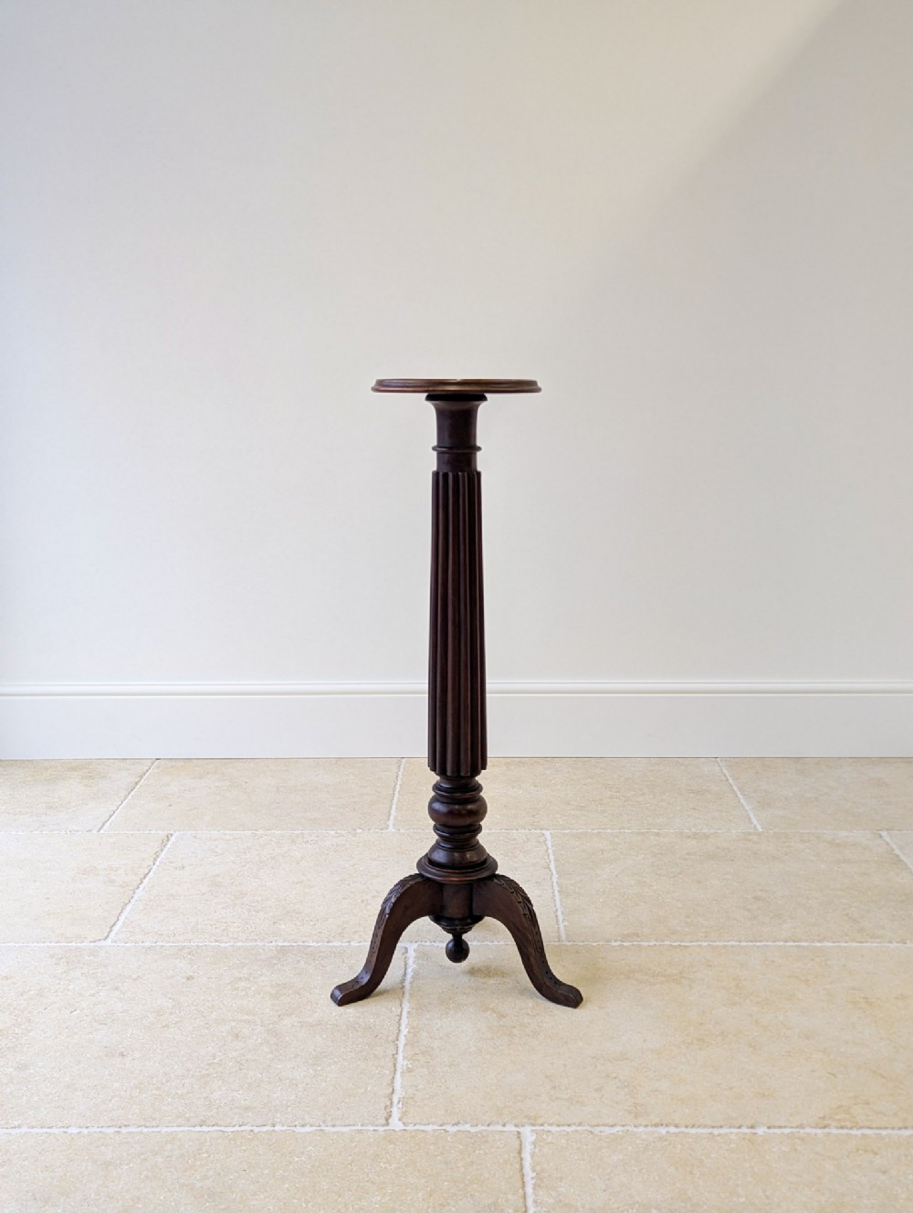 A tall William IV dark mahogany torchere featuring a circular moulded top, a reeded turned column stem, and a tripod base with carved legs.