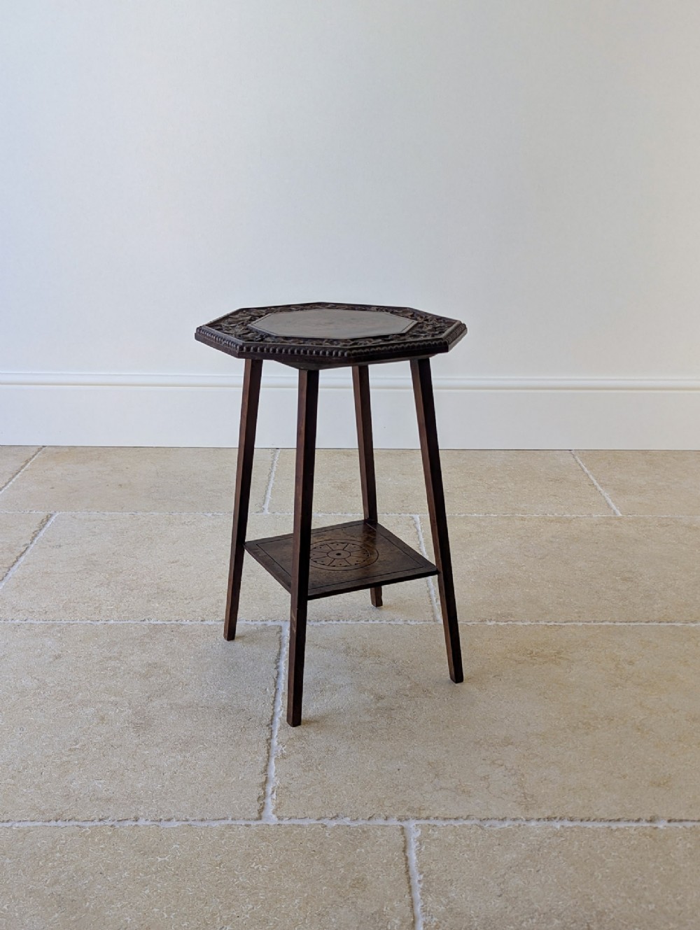 An antique dark walnut octagonal occasional table featuring a carved outer border, splayed legs, and a lower square tier with incised geometric motifs.